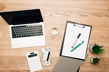 Top view of laptop, dollar banknotes with calculator and credit card on wooden table