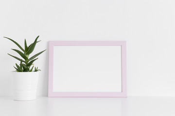 Fototapeta na wymiar Pink frame mockup with a aloe vera in a pot on a white table.Landscape orientation.