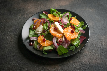 Detox salad with tangerines, mozzarella, herbs, pomegranate seeds and nuts on a dark background. Free copy space.