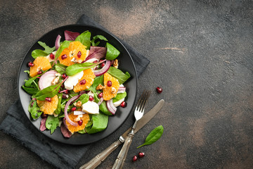 Detox salad with tangerines, mozzarella, herbs, pomegranate seeds and nuts on a dark background....