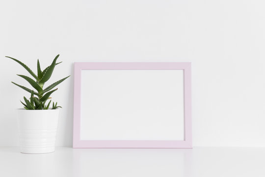 Pink frame mockup with a aloe vera in a pot on a white table.Landscape orientation.