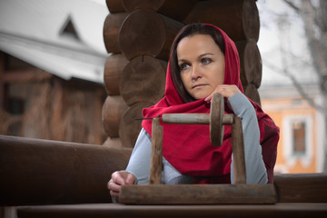 A girl in a red scarf on her head sits on the street in a gazebo of logs