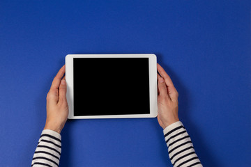 Female hands holding digital tablet computer on navy blue background. Top view