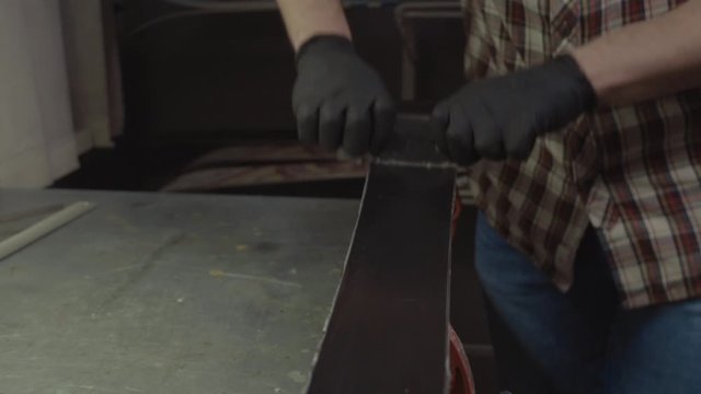 Ski maintenence. Removing excess wax from race ski base plastic scraper. Ski service and repair. Winter shop worker doing base repair. Rental workshop service. Repairman In Workshop Ski Service