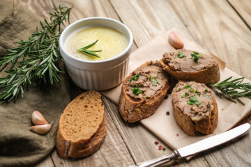 Fresh homemade chicken liver pate in ceramic bowl or ramekin and baguette slices with pate with herbs and garlic on a rustic wooden background. Top view.