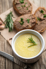 Fresh homemade chicken liver pate in ceramic bowl or ramekin and baguette slices with pate with herbs and garlic on a rustic wooden background. Top view.
