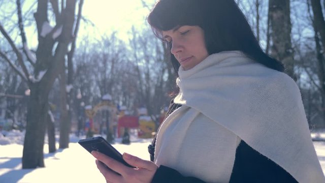 Happy Smiling Beautiful Girl Using Smart Phone. Sunny Day In Snow Covered City Park. Slow Motion 30 fps 0.5 normal speed 60 fps