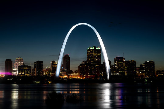 St Louis Gateway Arch brightly lit and shining at night, city skyline in background, reflecting in Mississippi River 