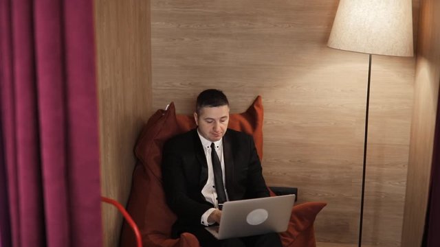 Overtime job concept. Careerist tired mature man working on laptop sitting in bean bag chair in office. Camera zooms in. Businessman, freelancer, manager, boss, chief making his job on computer.