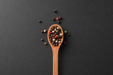 Wooden spoon with pepper spice on black background, top view