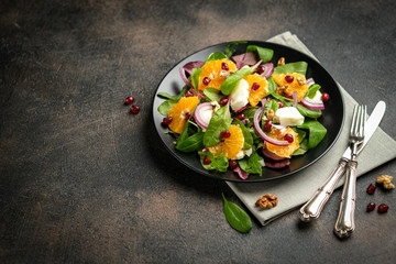 Detox salad with tangerines, mozzarella, herbs, pomegranate seeds and nuts on a dark background. Free copy space.