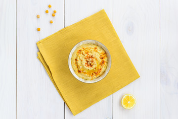 Hummus with pine nuts, paprika and butter in a bowl on a wooden table. Horizontal orientation, top view.