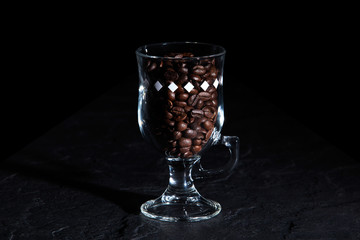 Transparent glass with fragrant coffee beans on a dark background.