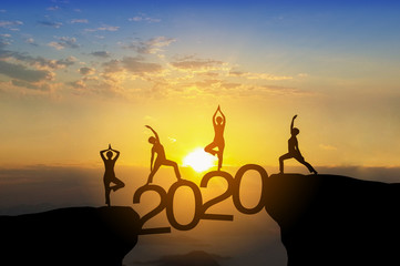 Silhouette image of happy teamwork yoga pose by standing on 2020 text and beautiful sky.