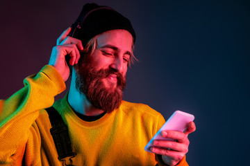 Calm, happy, using phone. Caucasian man's portrait on gradient studio background in neon light. Beautiful male model with hipster style. Concept of human emotions, facial expression, sales, ad.