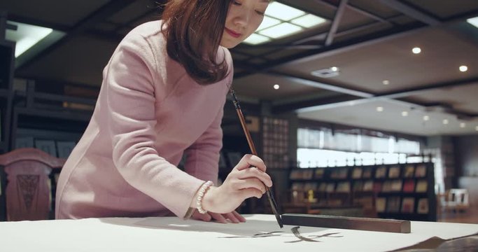 Chinese brush writing learner practicing handwriting in retro library, young woman enjoying arts of brush writing, arts lover studying chinese brush pen the arts of Chinese brush calligraphy
