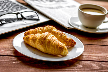 Business lunch with croissant and laptop on wooden desk