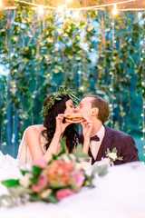 Stylish wedding couple eating fastfood and kissing, bride holds tasty burger in hands. Wedding...