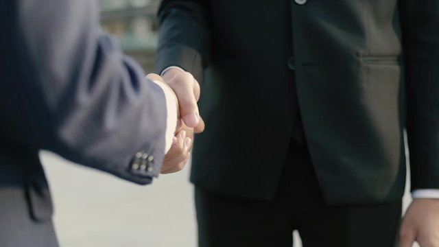 Close up hands asian business people in a black suit shaking hands partnership deal while standing outside on the street near a big office building urban.