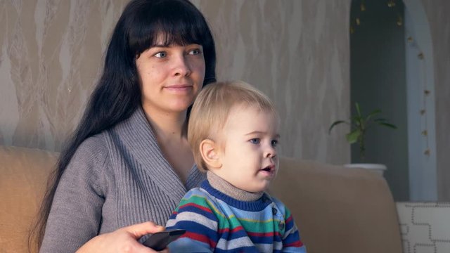 Pretty Mother With Remote Control in Hand and Cute Child Watching Personal Home Video. Sitting On Sofa Couch In Room. Slow Motion 30p 0.5 Real Time Speed
