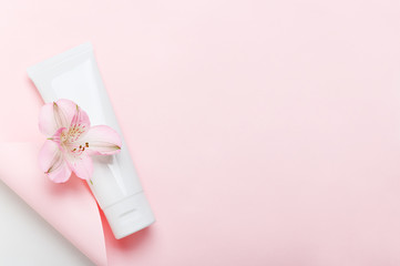 Obraz na płótnie Canvas Feminine hygienic product tube on pastel pink background. Shampoo, hand cream, toothpaste white package side view on paper sheet with scroll. Skincare, facial creme, moisturizer with place for text