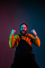 Crazy happy celebrating, winning. Caucasian man's portrait on gradient studio background in neon light. Beautiful male model with hipster style. Concept of human emotions, facial expression, sales, ad