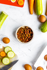 dry food for dogs, eggs and vegetables on kitchen background top view