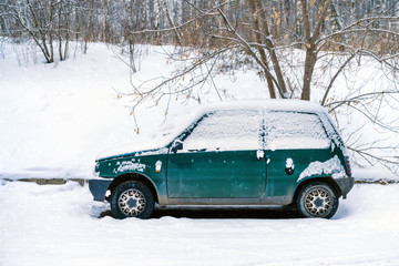 an old abandoned little green car covered with snow strewn. parked on the edge of the woods in winter