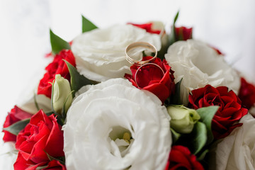 Gold wedding rings of the bride and groom on red roses and white eustoms close up. Symbol of love and loyalty