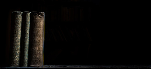 Old book on wooden bookshelf over black background. Vintage book covers still life on dark backdrop. - obrazy, fototapety, plakaty