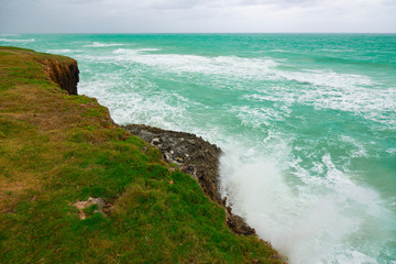Fototapeta na wymiar Ocean blue waves crashing on green rocks during cloudy day in Varadero, Cuba