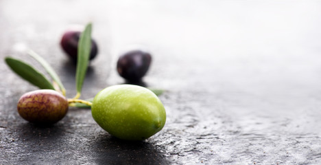 Closeup of fresh olive fruit on dark textured background with copyspace. Black and green organic olives with leaf.