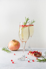 Pomegranate Christmas cocktail with rosemary, sparkling wine on white table. Xmas Holiday drink.