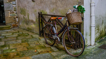 Old bicycle parked on a street in an old town, with a basket of gifts and flowers on the handlebars.