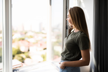 Young woman opening window in living room at home