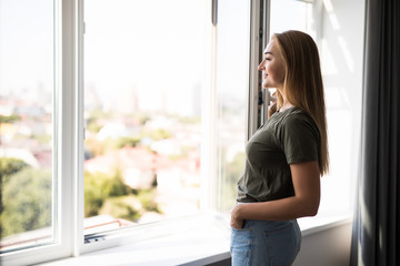 Young woman opening window in living room at home - Powered by Adobe