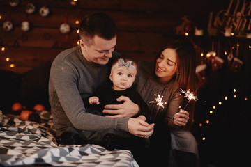 cute young family, dad, mom and baby girl with sparklers on bed with Christmas background behind.