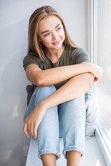 Beautiful young woman sitting at windowsill at home