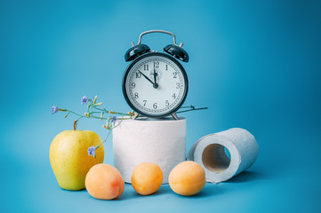 Alarm clock, fruits and toilet paper on a blue background. Natural remedy for constipation. The concept of healthy digestion