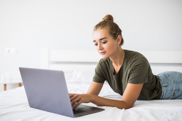 Smiling woman in front of her laptop lying on the bed.