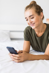 Relaxed young woman at home reading a text message in her bed