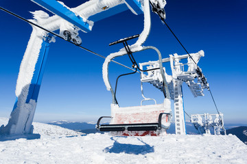 Empty ski lift covered with frost and snow with mountains at background