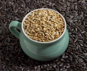peeled sunflower seeds sprinkled in a small colored bowl on a background of unpeeled black sunflower seeds