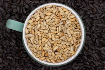 peeled sunflower seeds sprinkled in a small colored bowl on a background of unpeeled black sunflower seeds