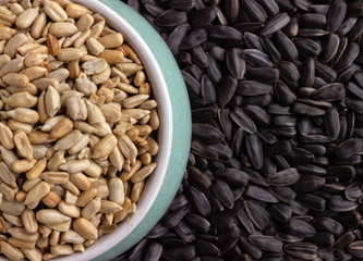 peeled sunflower seeds sprinkled in a small colored bowl on a background of unpeeled black sunflower seeds