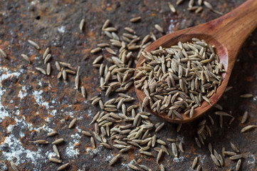 Cumin seeds in wooden spoon on a textured background