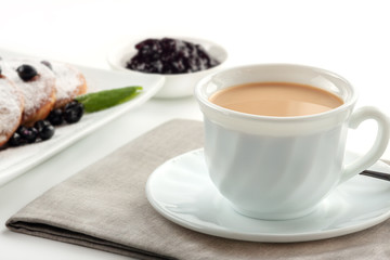 A Cup of coffee with milk and a plate with a pancakes is on the table.