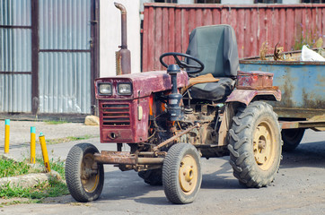 Obraz premium A small old mini tractor with a trailer stands on a rural street