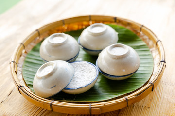 Top view Thai Desserts Coconut Milk Custard on wooden table, cup of Khanom Thai in small white porcelain cup or Thai traditional sweet called Kanom Tuay put inside served on banana leave in Thailand.