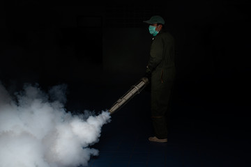 Man work fogging to eliminate mosquito for preventing spread dengue fever in a dark room